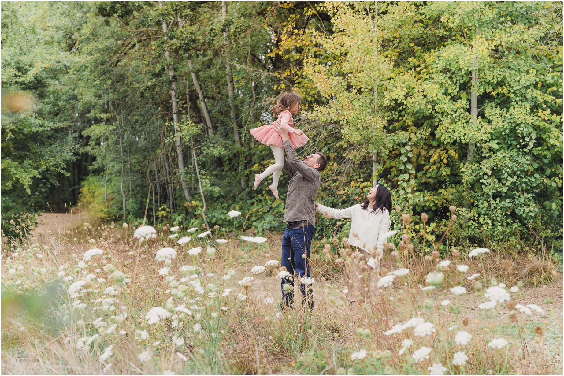 Tigard Family Photographer takes photographs of a family as a father lifts his daughter over queen Anne's lace