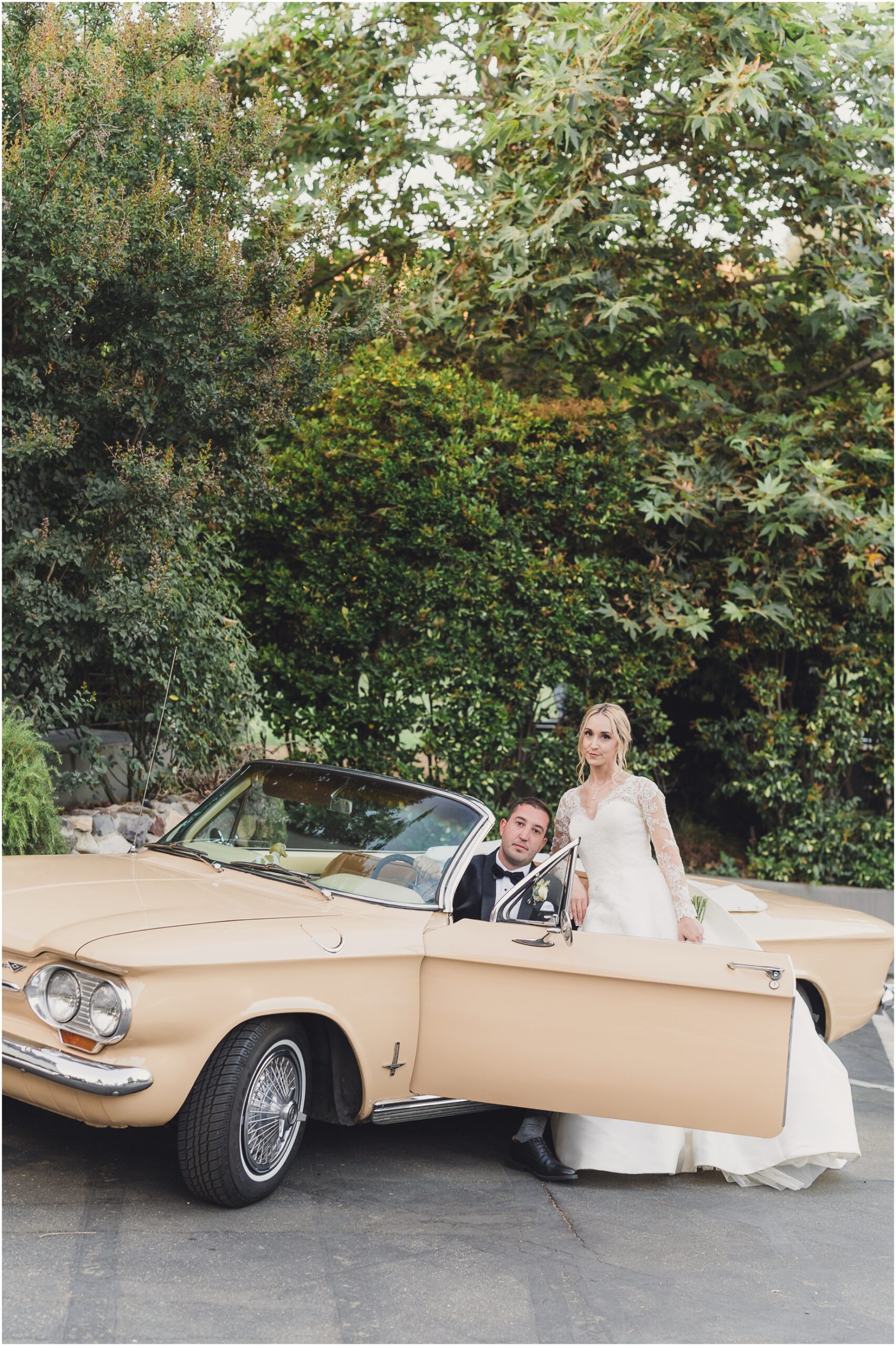 A groom sits in a classic car as his bride leans near to him