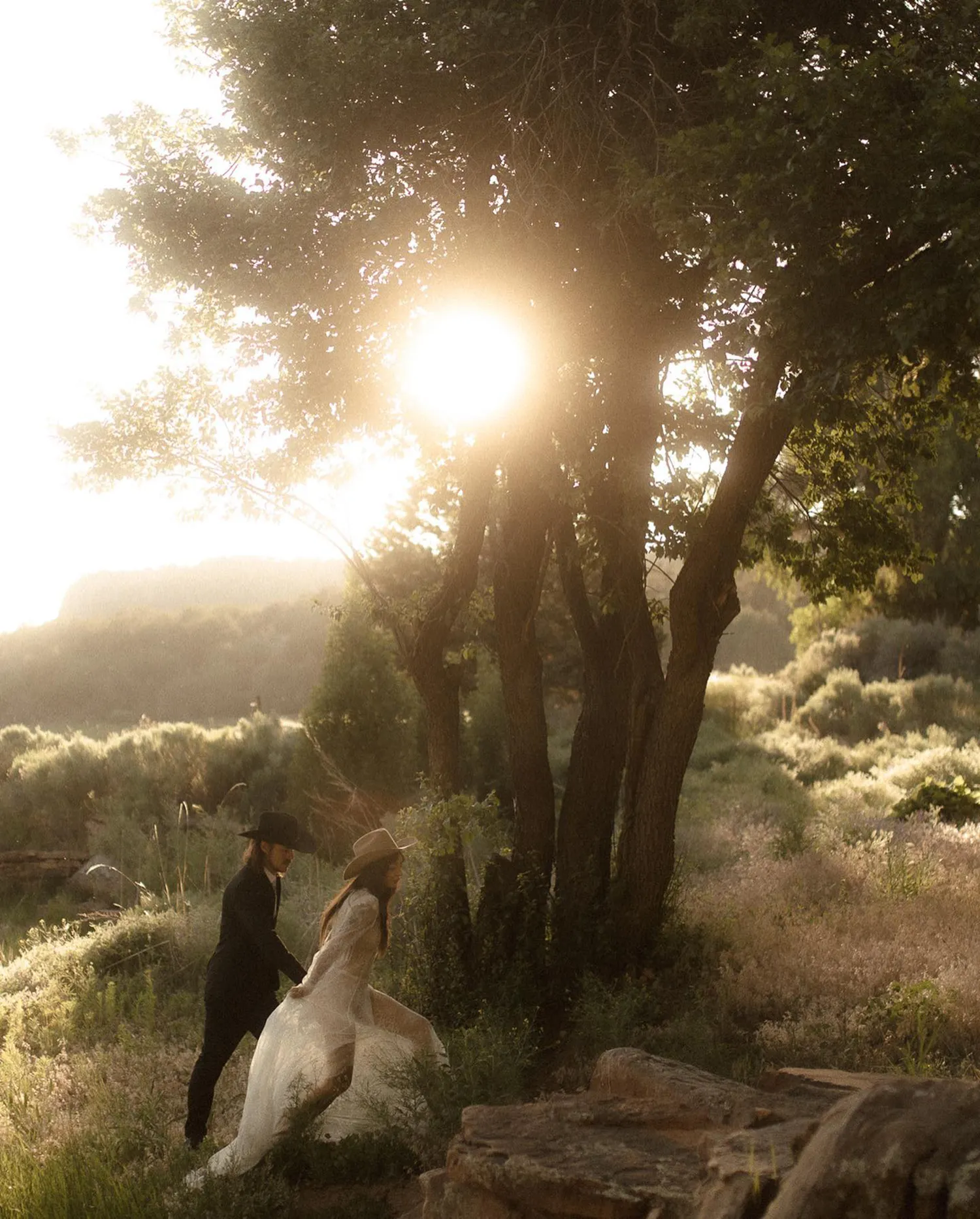 Top Wedding Photographers of 2024 Mari Trancoso capture a magical moment with a bride and groom playfully running through a sun-drenched grove, the sunlight creating a stunning halo effect around them, exemplifying the enchanting quality of outdoor weddings.
